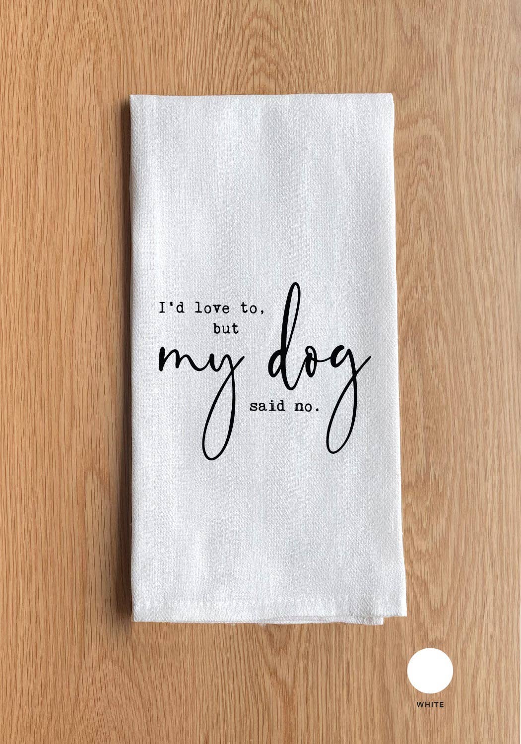 A versatile kitchen towel called "I'd love to, but my dog said no," made from 100% cotton, features black text and is shown placed on a wooden surface.