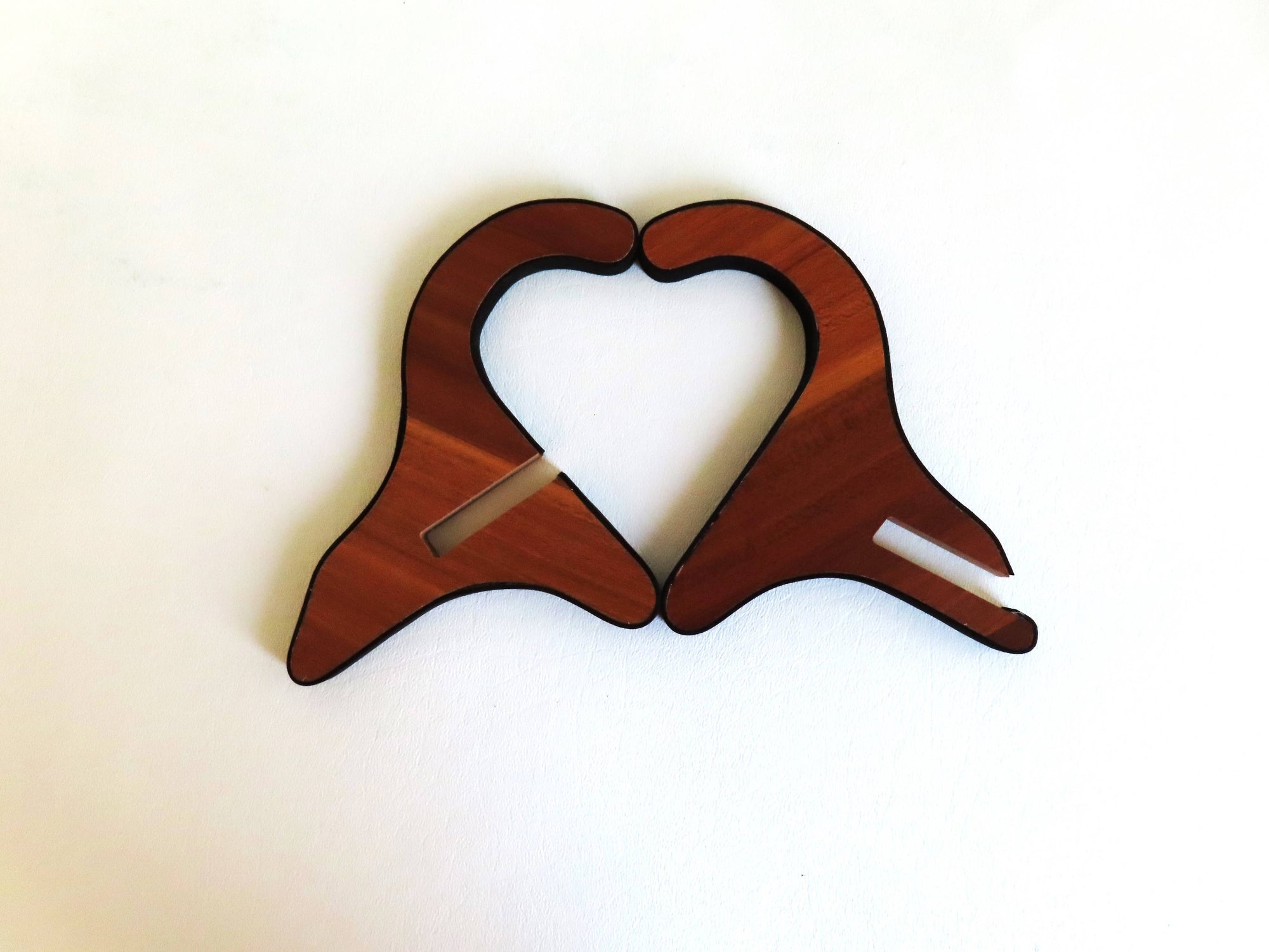 Two wooden objects with curved shapes placed together to form a heart against a white background. Each piece has a small, rectangular cutout, perfect for holding your Kalimba Stand - Wood or as an elegant display stand.