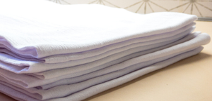 A stack of 100% cotton white cloth diapers on a table, perfect as a gift or for use as Arkansas Tea Towels.