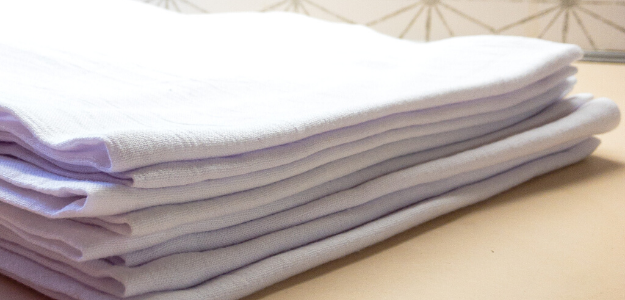 A stack of neatly folded white Y'all Tea Towels, perfect for a housewarming gift, placed on a light-colored surface.