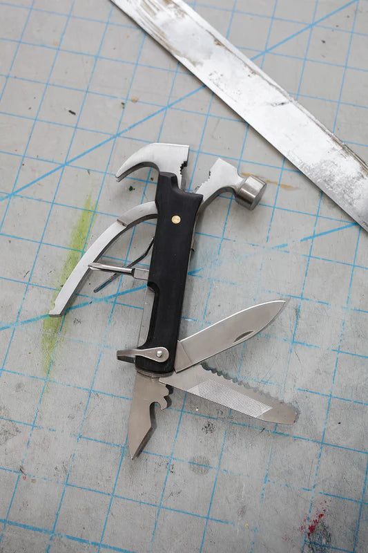 A Black Wood Multi Hammer Tool with open tools lying on a blue cutting mat, next to a metal ruler and labeled "10 Tools in 1!