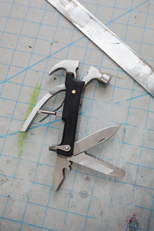 A Black Wood Multi Hammer Tool with open tools lying on a blue cutting mat, next to a metal ruler and labeled "10 Tools in 1!