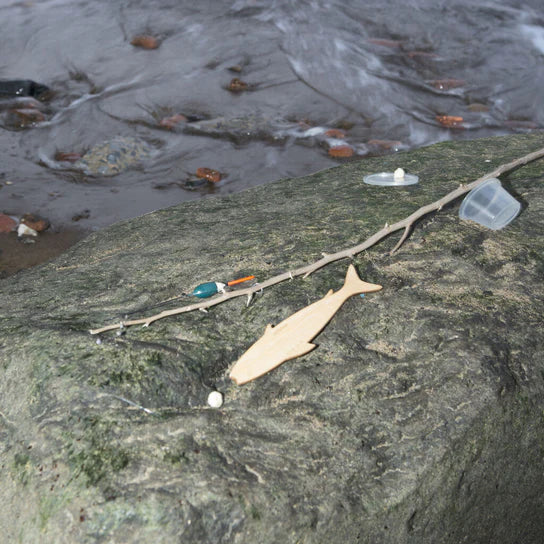 Plastic waste and debris, including a Huckleberry Fishing Kit, scattered on a wet rock by a water stream.