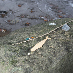 Plastic waste and debris, including a Huckleberry Fishing Kit, scattered on a wet rock by a water stream.