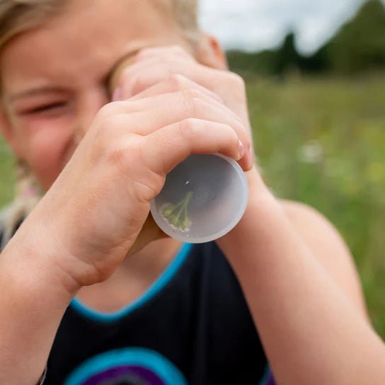 Child looking through a Huckleberry Kaleidoscope outdoors with a blurred green background, imagining stars and planets like young artisans sculpting the galaxy.