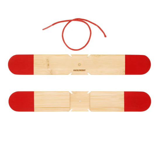 Two wooden bracelets with red ends and a red string laid out on a white background. The top bracelet has the string looped in a circle above it, reminiscent of the curve of a boomerang. The brand name "Huckleberry Pocket Boomerang" is visible.