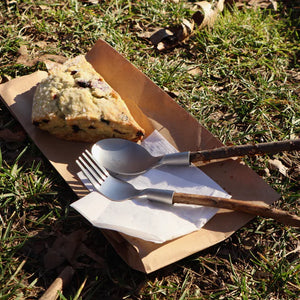 A slice of Huckleberry Forest Cutlery on a paper plate with a utensil crafting kit fork and knife on grass, partially in sunlight.