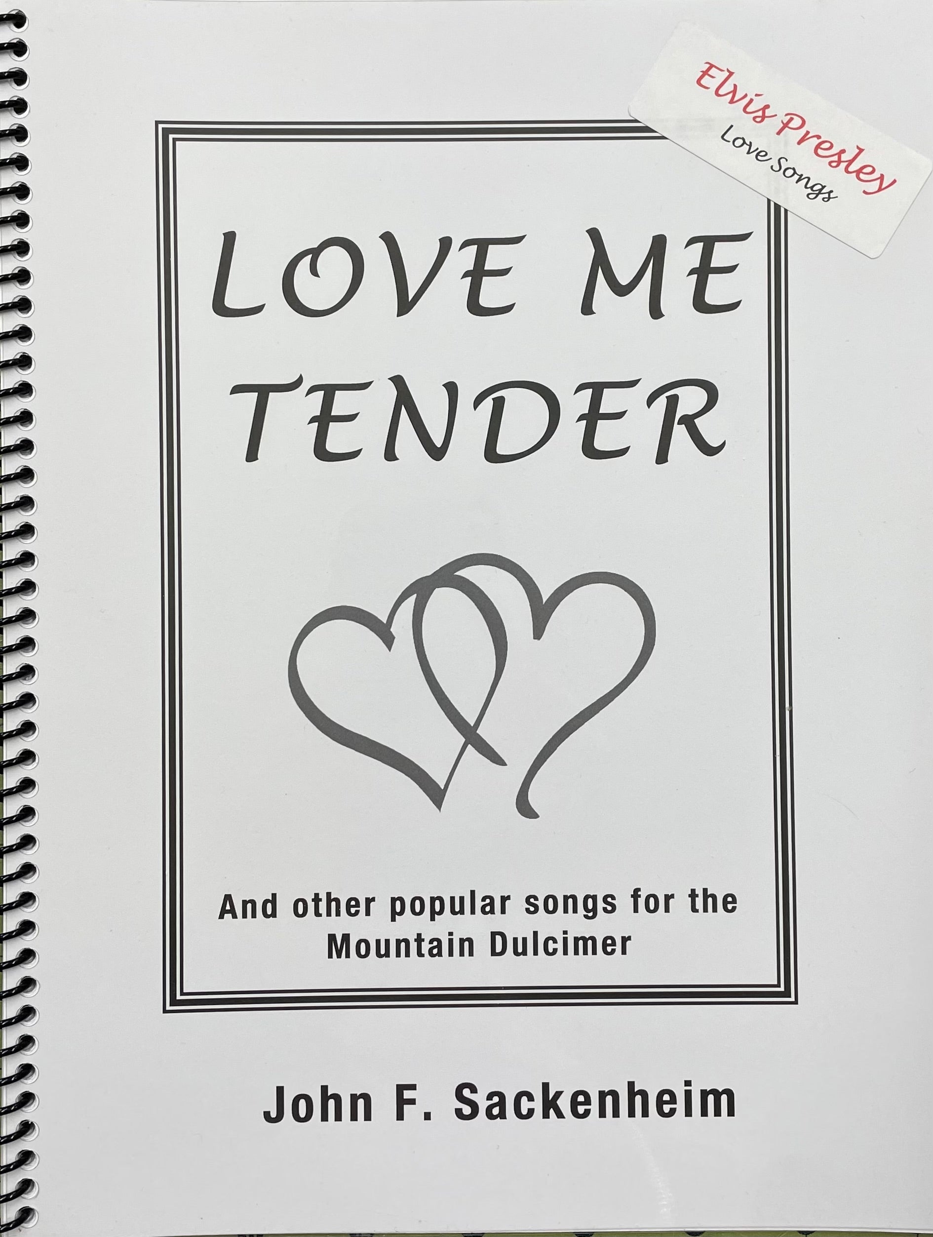 A spiral-bound book titled "Love Me Tender" by John Sackenheim, focusing on DAd tuning for the mountain dulcimer and covering popular songs including a note on "Elvis Presley Love Songs".