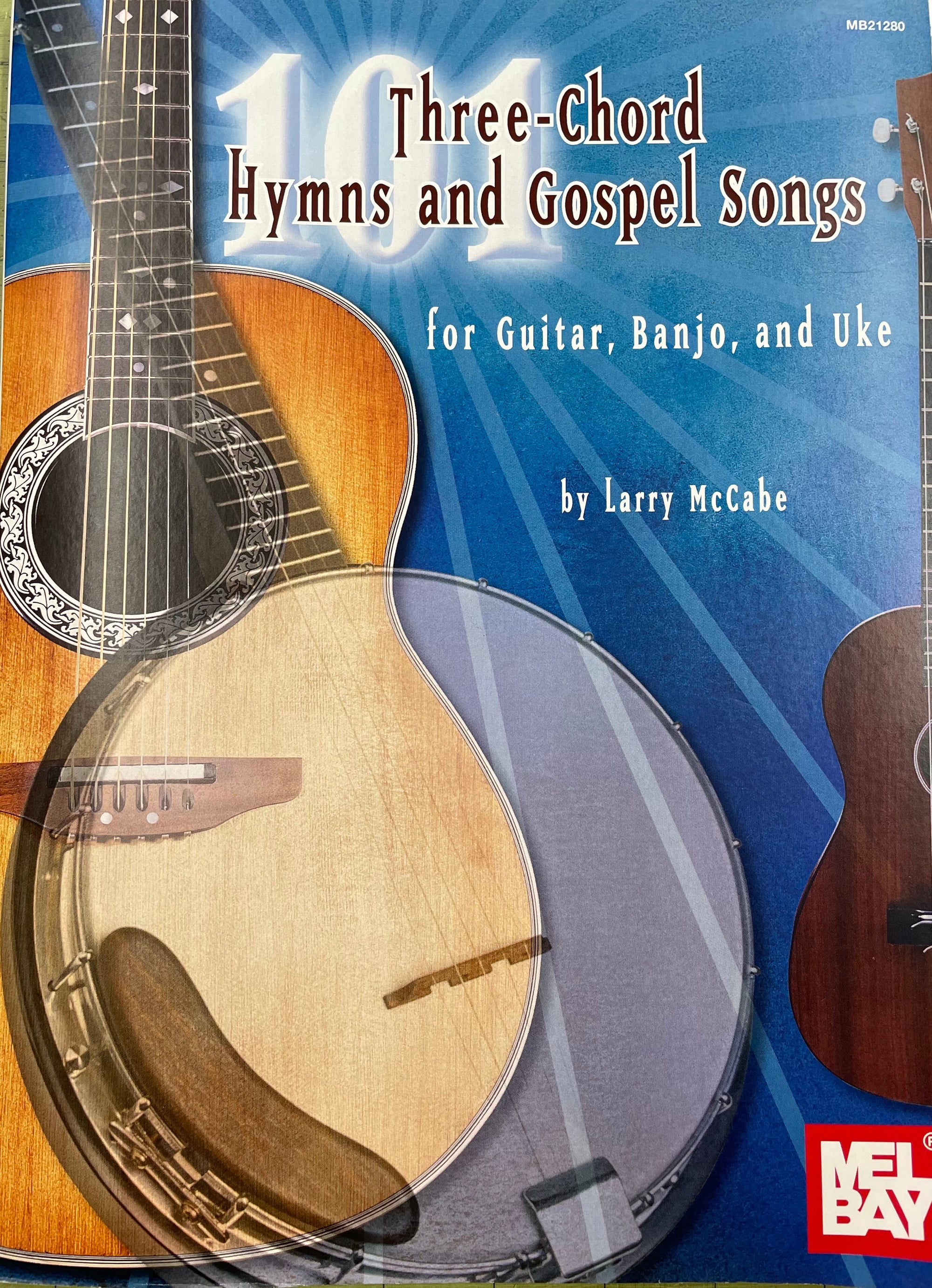 A music book titled "101 Three-Chord Hymns & Gospel Songs for Guitar, Banjo, and Uke" by Larry McCabe featuring images of stringed instruments on the cover and designed to
