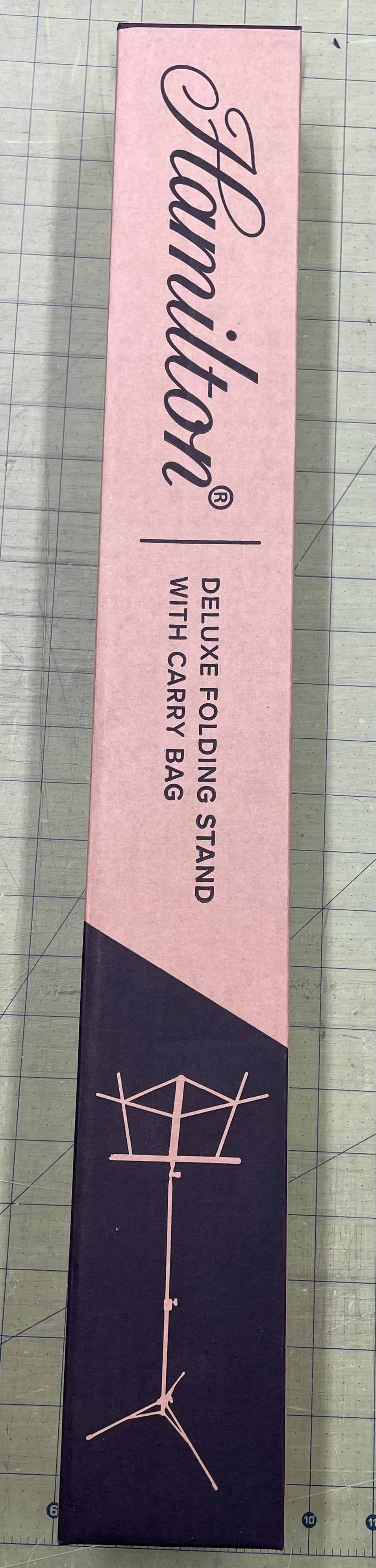 A long, rectangular cardboard box with branding "Deluxe Folding Music Stand with Carry Bag," "6 magnetic effortless glam eyelashes," and graphics of eyelash designs and a music stand symbol.