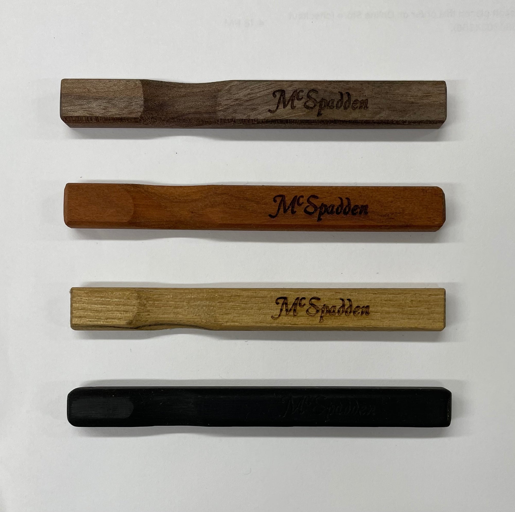 Four McSpadden Noters in different wood finishes, each intricately engraved with "McSpadden." 