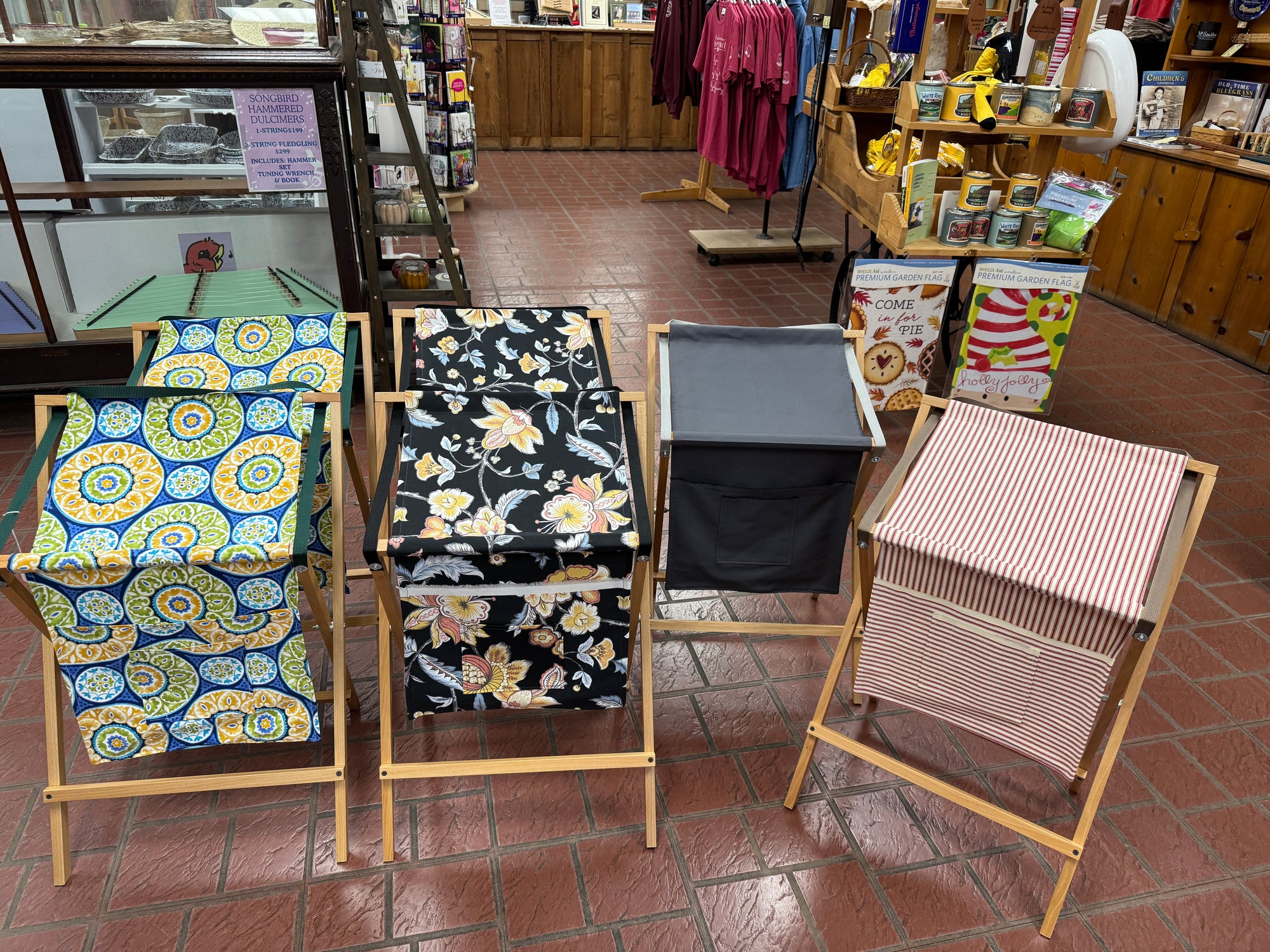 Four handmade Sling Music Stands with fabric bags—blue and yellow, floral, plain gray, and red striped—are displayed on a tiled floor indoors, each featuring a stylish and unique design for organizing sheet music.