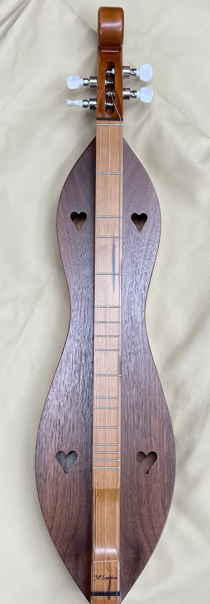 A handcrafted 4 String Ginger, Scrollhead Hourglass dulcimer with cherry back and sides and a walnut top rests on a cream-colored surface, showcasing the charm typical of Appalachian instruments.