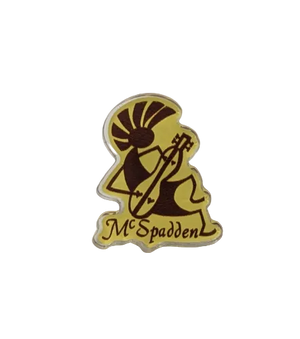 Yellow and brown McSpadden Kokopelli Pin depicting a stylized figure playing a mountain dulcimer, with the word “McSpadden” written below the illustration.