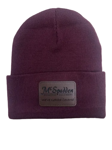 The Beanie Knit Cap with McSpadden Logo Patch is a maroon knit beanie featuring a folded brim and a rectangular patch that reads "McSpadden" and "We've Gotcha Covered.