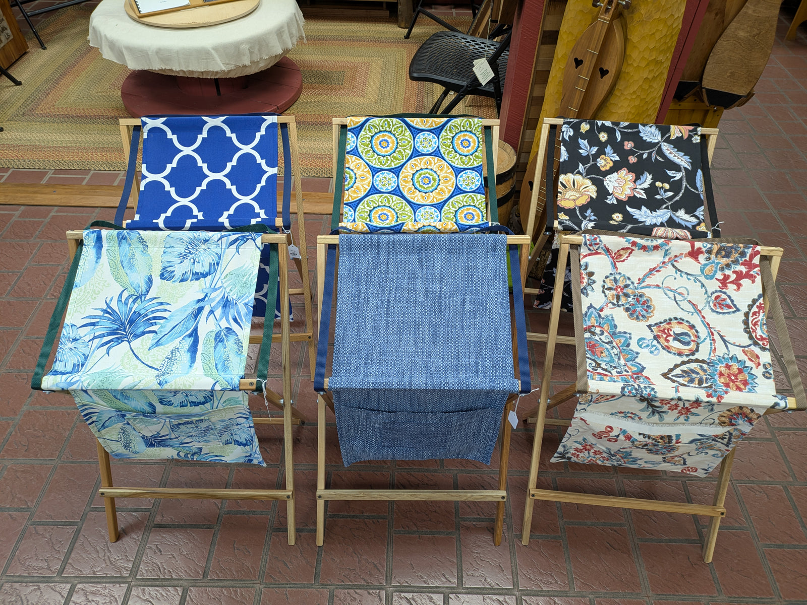 Five wooden folding chairs with colorful patterned fabric seats are arranged in a row beside a Sling Music Stand on a tiled indoor floor.
