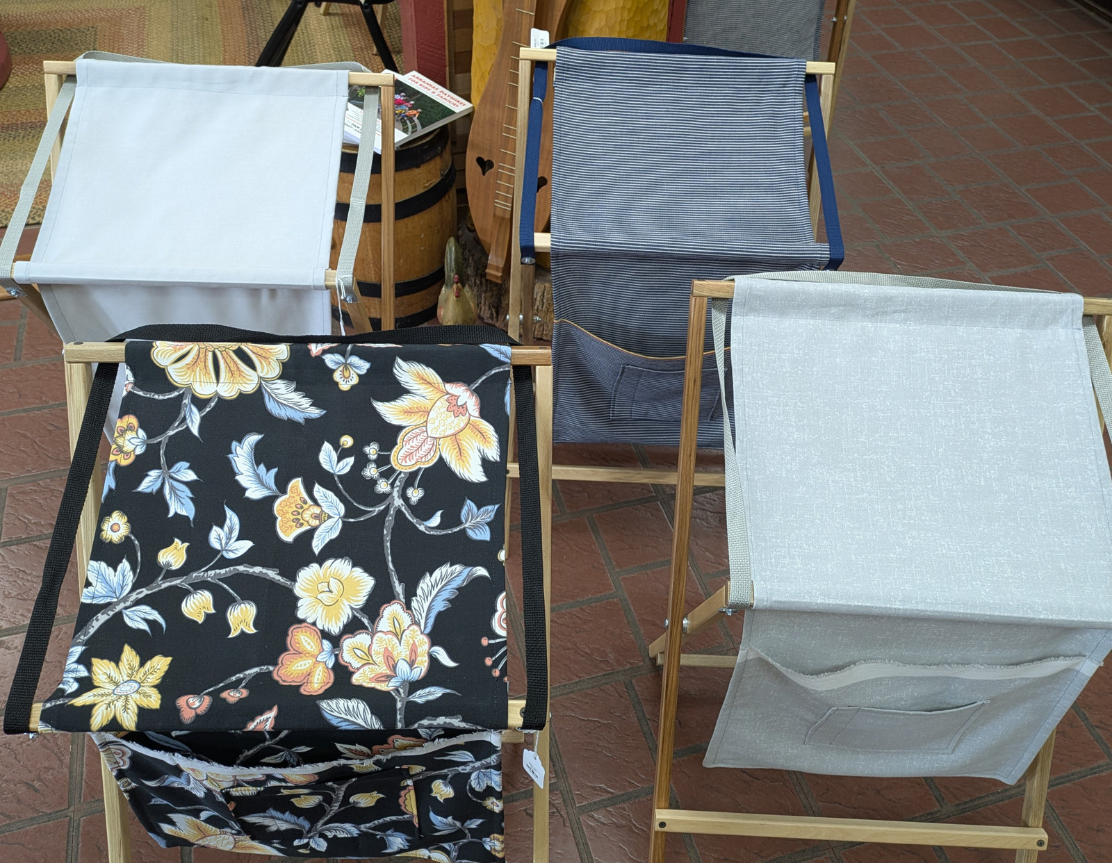 Four Sling Music Stands are displayed on a tiled floor, each featuring fabric bags in floral, solid, and striped designs—perfect for use as stylish music stands or unique instrument accessories.
