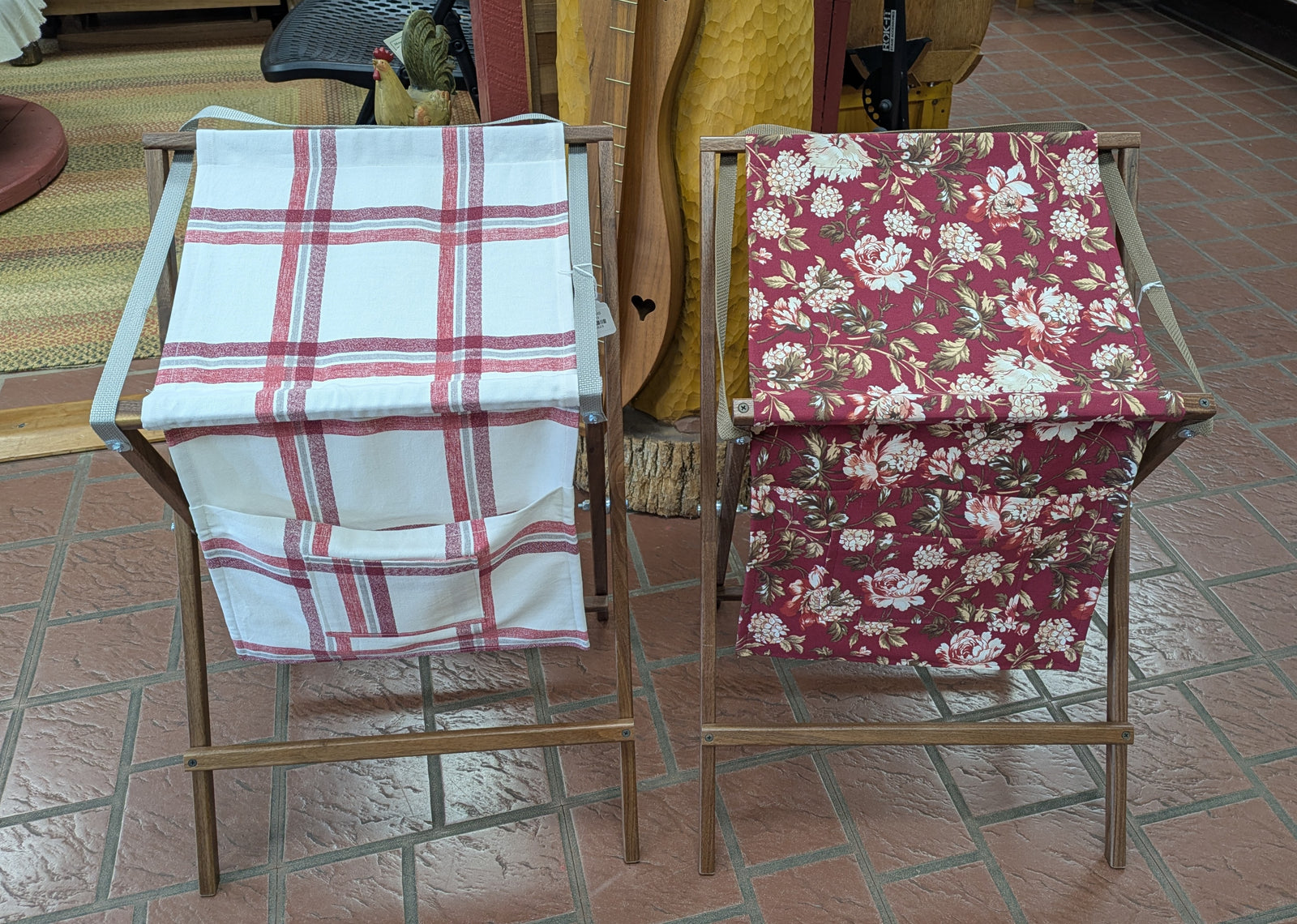 Two Sling Music Stands, their wooden frames reminiscent of a handmade towel rack or echoing the elegant curves of a music stand, display fabric—one draped with a red and white plaid pattern, the other adorned with red florals. Both rest on an indoor tiled floor.