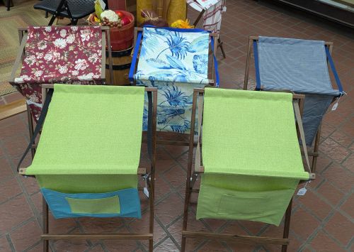Five Sling Music Stands, fabric-covered and adorned with various patterns and colors, reminiscent of a handmade music stand’s crafted charm, are arranged in two rows on a tiled floor indoors.