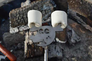 Two marshmallows roasting over a campfire on a telescopic Animal Roaster shaped like a cartoon bear face.