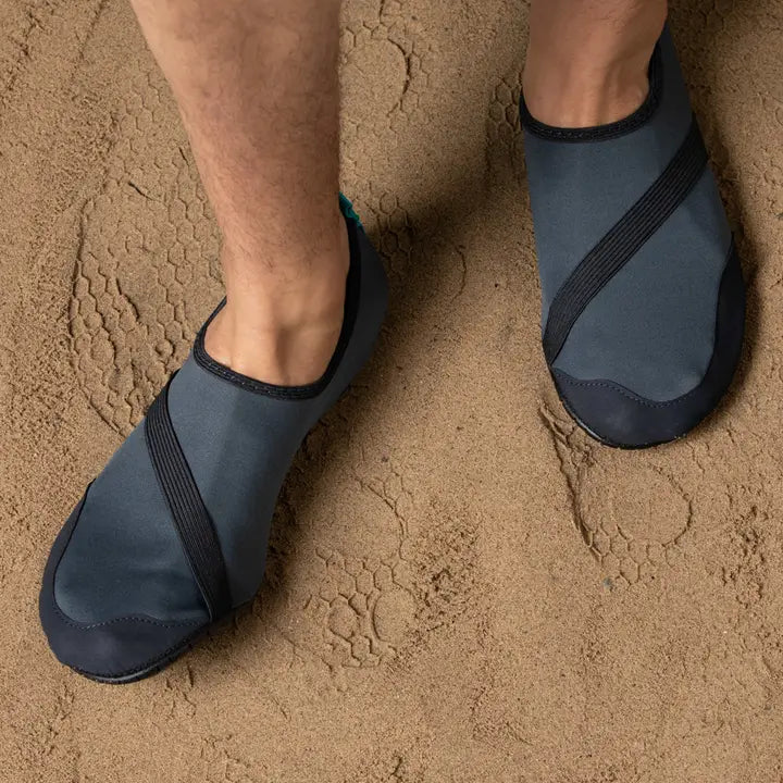 A person wearing Men's Classic Fitkicks stands on a sandy beach, with visible sand texture around their feet.