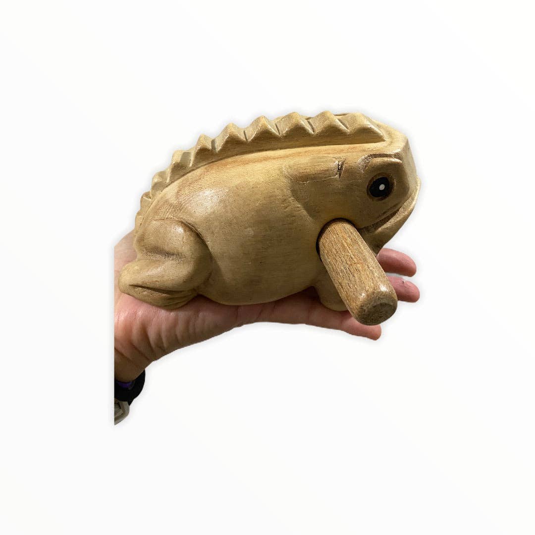 Hand holding a Natural wooden frog percussion instrument, handmade in Thailand with quality craftsmanship, featuring a stick inserted into its mouth for creating sound.