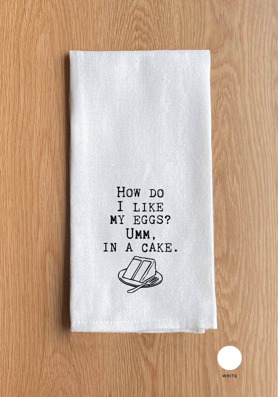 Resting on a wooden surface, the "How do I like my eggs? Umm, in a cake." kitchen towel showcases a humorous phrase alongside an illustration of a cake slice and fork. Crafted from 100% cotton, this versatile towel serves as an ideal handmade hostess gift.