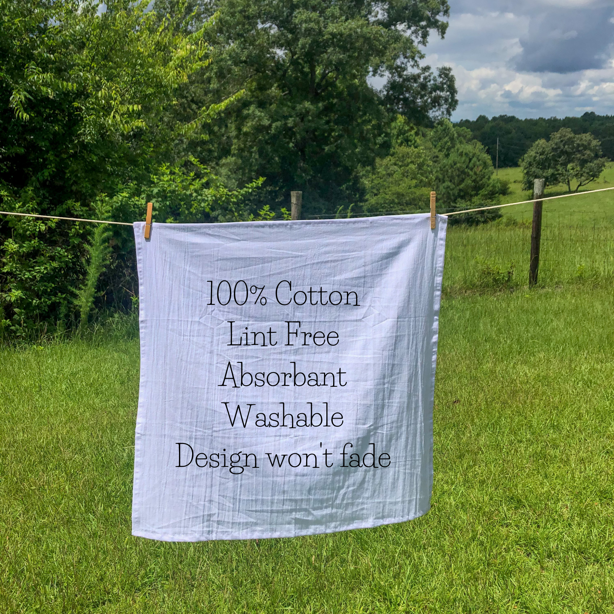 A white "Coffee Homeschool Repeat Tea Towel" with text detailing its features hangs on a clothesline in a grassy outdoor setting. The text reads: "100% Cotton, Lint Free, Absorbent, Washable, Design won't fade." Perfect as a back-to-school gift for teachers or students.