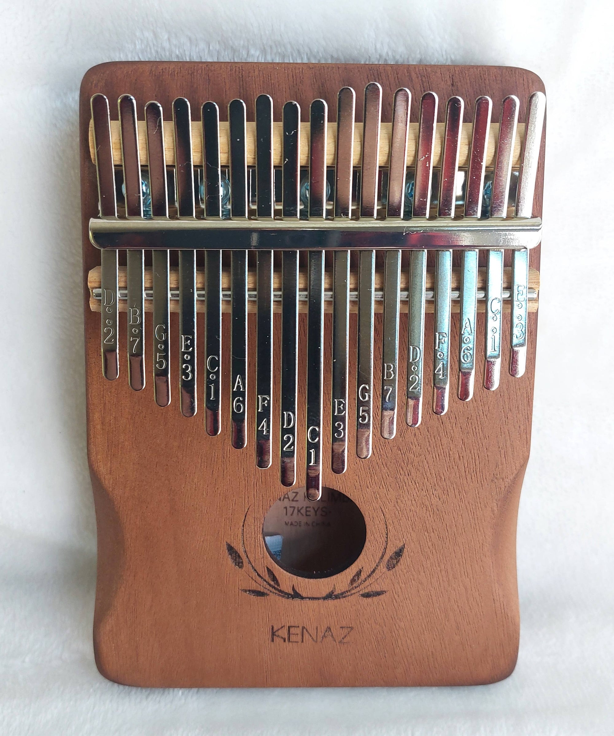 A wooden 17-key Kalimba Musical Instrument with tines labeled with musical note names, photographed on a white background.