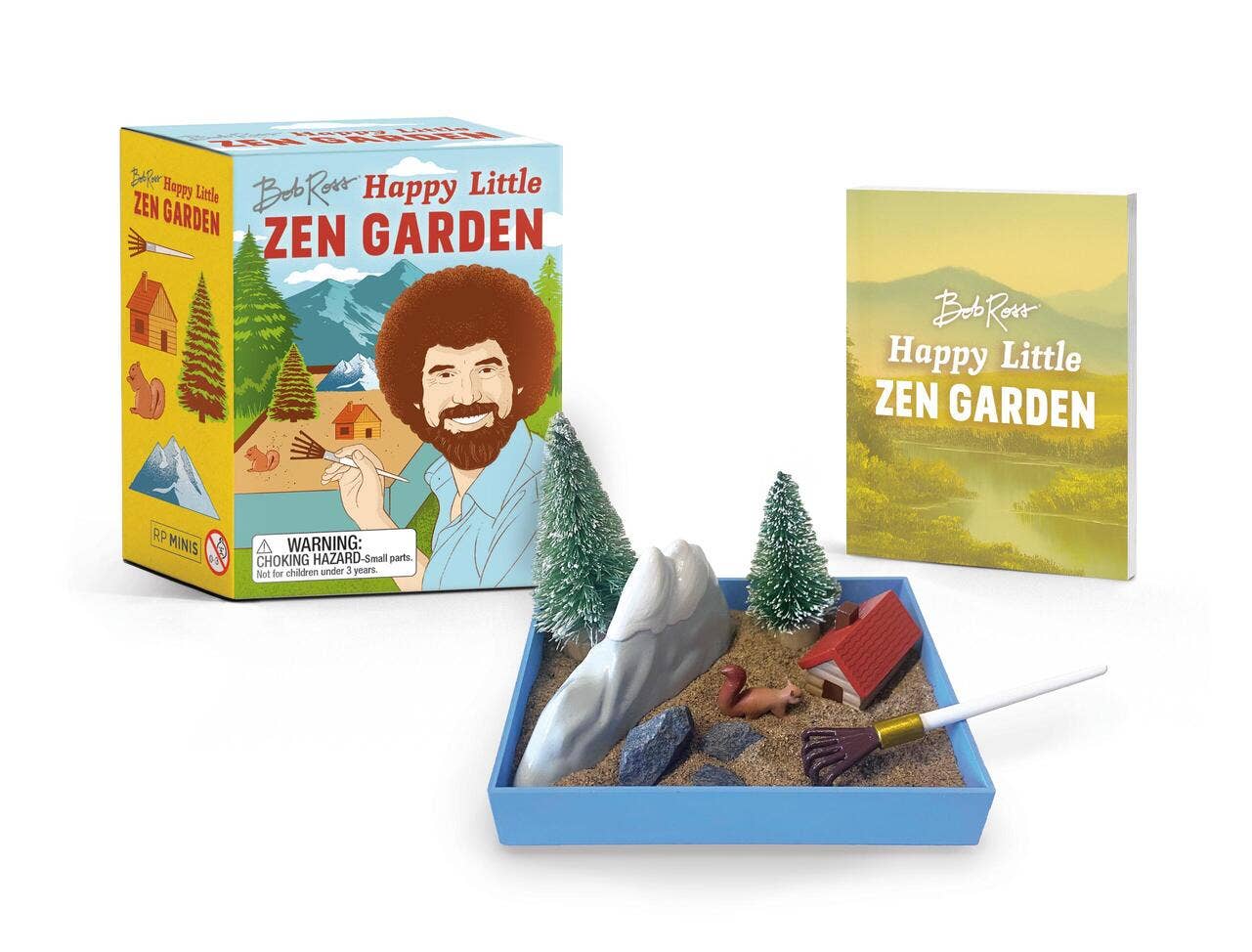 Box and contents of the Bob Ross Happy Little Zen Garden, a delightful desktop accessory featuring a mini Zen garden with sand, rocks, trees, red cabin, miniature rake, and an included booklet for stress relief.