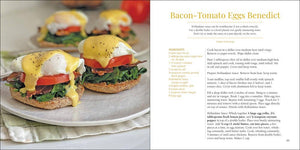 An open Eggs cookbook displaying a recipe for bacon-tomato eggs benedict on a white surface, alongside a plate with two prepared servings of the dish.