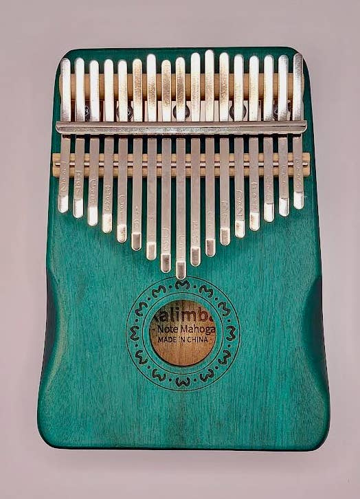 A close-up of a green wooden Kalimba Musical Instrument with metal tines, featuring a branded emblem in the center reading "kalimba mbira manocha made in China.