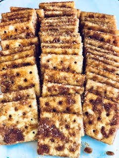 A neatly arranged stack of crispy, seasoned square crackers with a hint of Snickerdoodle Cracker Seasoning on a white background.