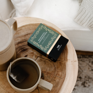 A cup of tea and a box of Meaningful Conversations with My Grandparents on a wooden table, perfect for intimate conversations and cherished moments with grandparents.