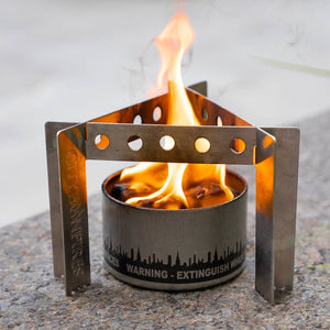 A Portable Camp Stove / Stand Combo with a visible flame burning inside a metal container, placed on a concrete surface.