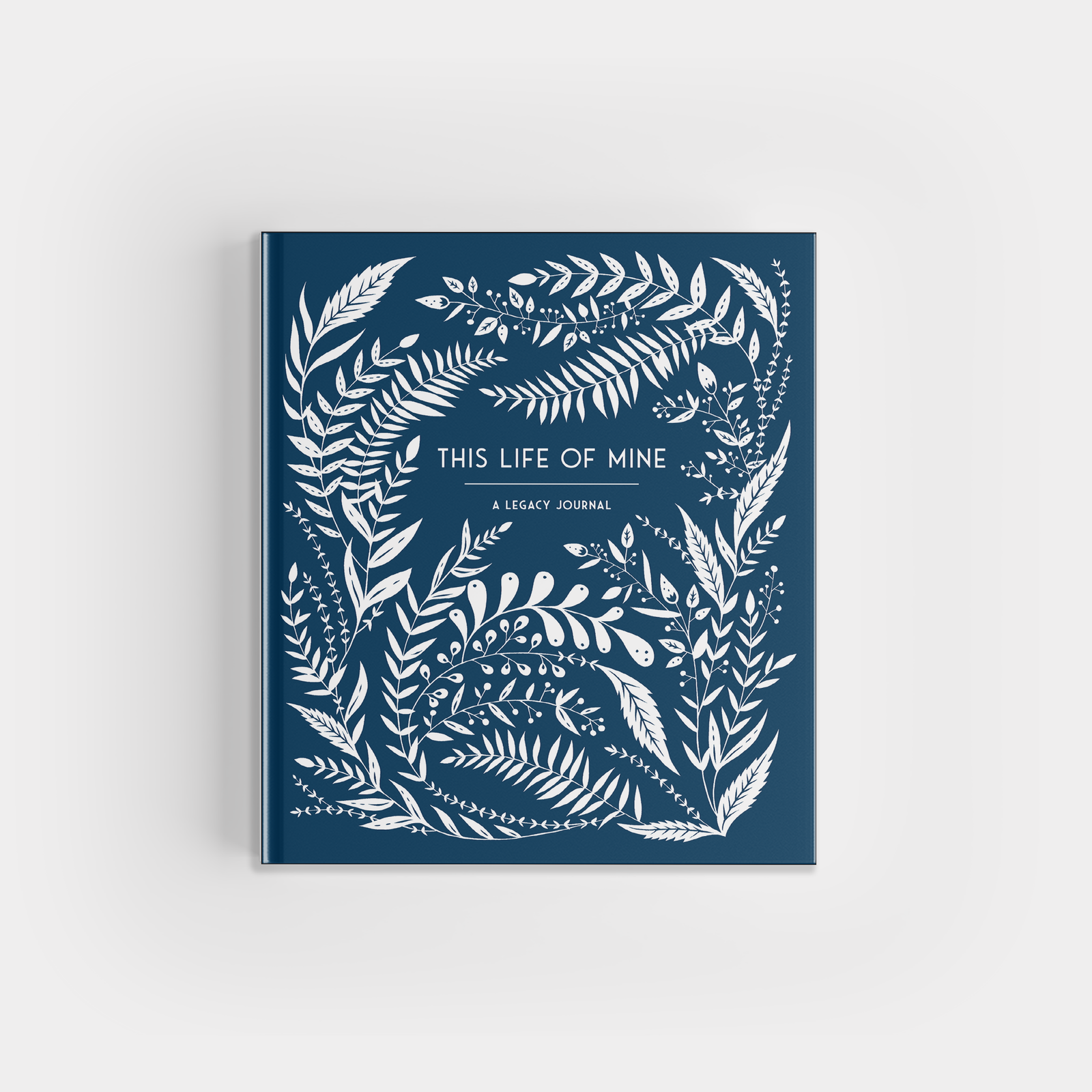 A blue hardcover book titled "This Life of Mine" featuring intricate white leaf and floral designs on the cover. This elegant keepsake journal is perfect for capturing reflections and memories, making it a thoughtful gift for any occasion.