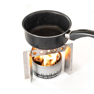 A small Portable Camp Stove / Stand Combo with an open flame heating a black saucepan, isolated on a white background.