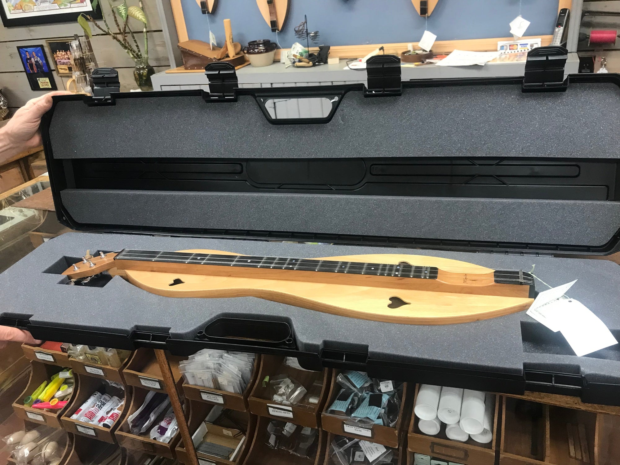 A person is holding a wooden lute in an Upgrade Hard Shell Dulcimer Case for enhanced protection.