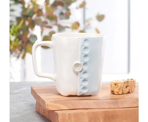 A handmade ceramic mug from the Studio M Coffee Mugs collection, featuring a unique button design in blue and white.