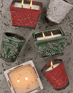 Several Holiday Bowl Swan Creek Candles in red, green, and white holders are lit and arranged on a gray textured surface.