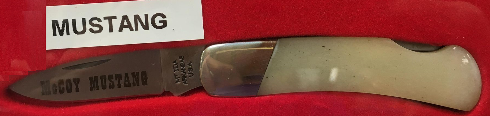 A lockback knife with the word McCoy Mustang engraved on its smooth white bone handle.