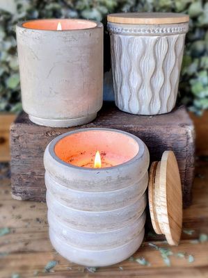 Three lit Swan Creek Parisian Courtyard candles in textured ceramic holders on a wooden surface, with one lid placed beside the corresponding candle, exuding a chic yet classic elegance.