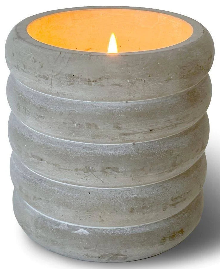A lit candle in the Parisian Courtyard Curvy Vase from Swan Creek Candles, featuring a round, ribbed, gray concrete holder with a smooth surface and visible texture.