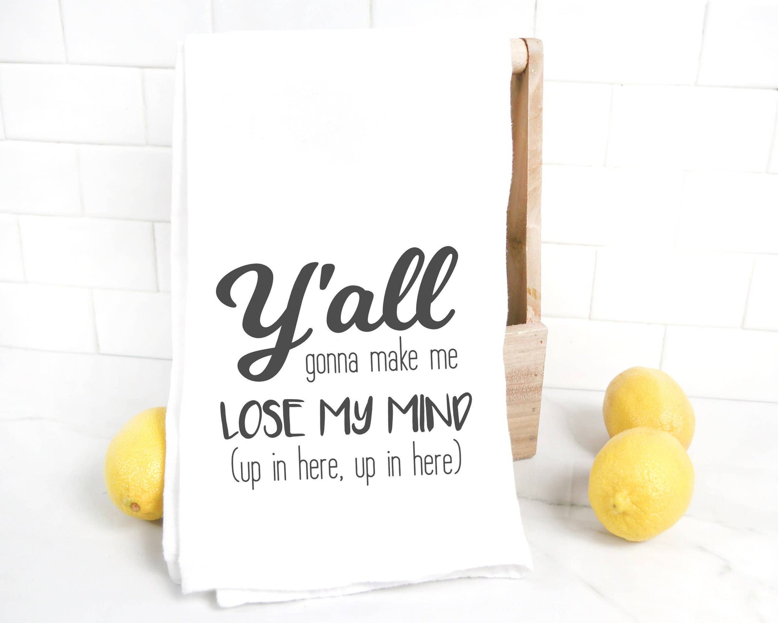 The discontinued "Y'all Gonna Make me Lose my Mind" tea towel is a white flour sack kitchen towel with lemons, decorated with the quote in stylish fonts using quality heat transfer vinyl.