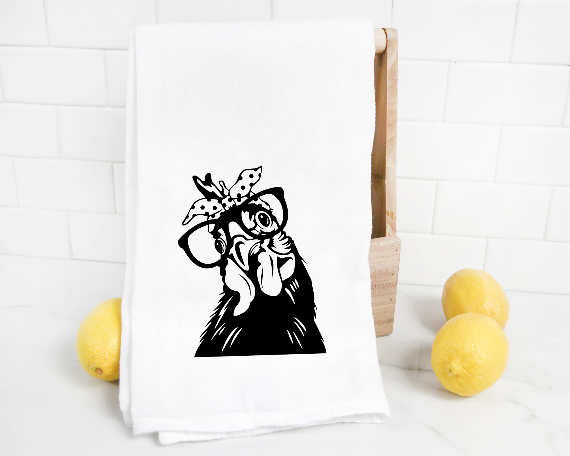 A white Funny Chicken Tea Towel with a black heat transfer vinyl illustration of a funny chicken wearing glasses, displayed on a countertop with lemons nearby.