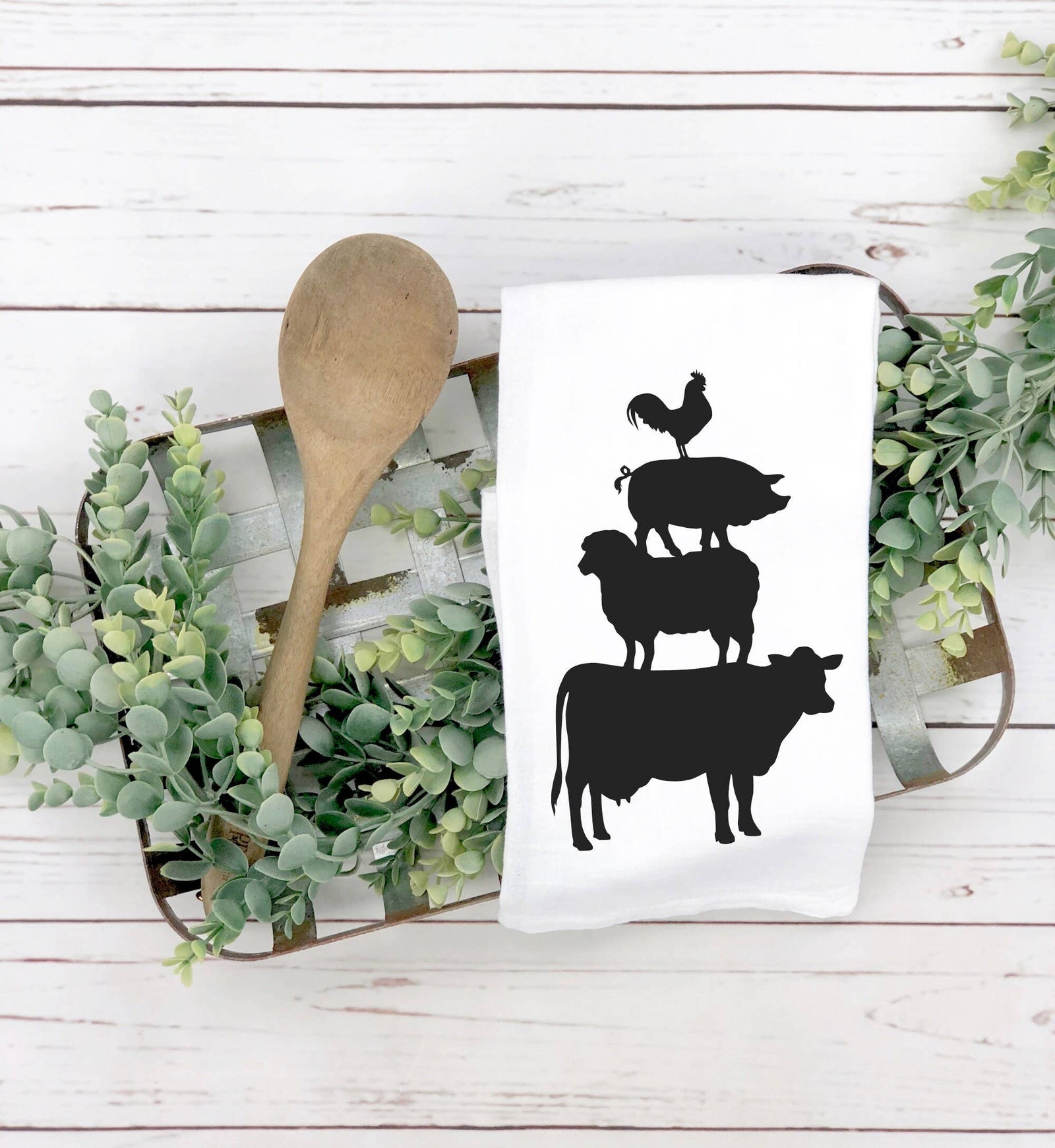 The discontinued Animal Stack Tea Towel is a farmhouse-style kitchen essential with black silhouettes of a cow, sheep, pig, and rooster stacked on white—ideal for display with greenery and a wooden spoon.