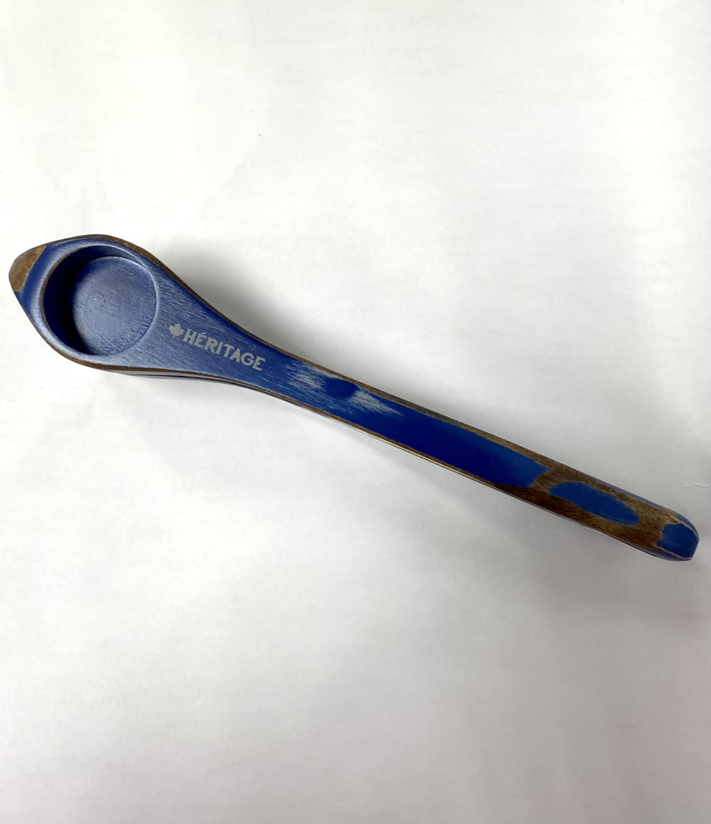 Blue measuring spoon labeled "Heritage Musical Spoons Large" from Canada on a white background.