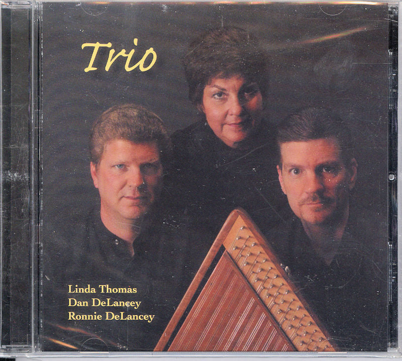 CD cover for "Trio by Linda Thomas, Dan and Ronnie DeLancey," showcasing three adults—two men and a woman—in dark attire, with a musical instrument prominently displayed in the foreground.