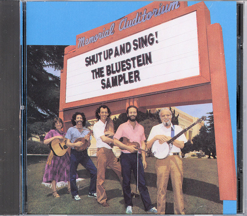 Five people with instruments stand in front of a sign that says "Shut Up and Sing! by Bluestein Family" at Memorial Auditorium.