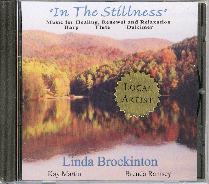 The CD cover of "In The Stillness" by Linda Brockinton showcases calming music ideal for healing and relaxation, featuring the harp, flute, and mountain dulcimer. It is set against a peaceful autumn lake scene, providing an ideal backdrop for tranquility and renewal.